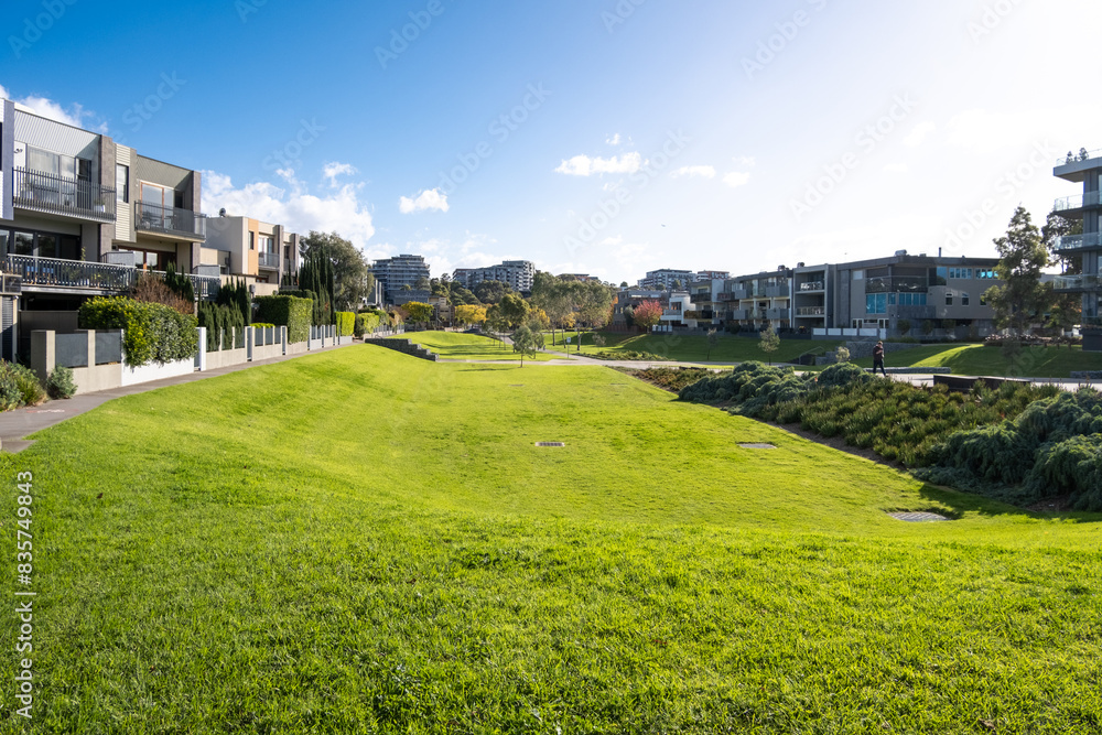 Background texture of a large green outdoor space in an urban park with storm drains surrounded by rows of residential houses and apartment buildings. A local neighbourhood in modern homes. Background texture of a large green outdoor space in an urban park with storm drains surrounded by rows of residential houses and apartment buildings. A local neighbourhood in modern homes.