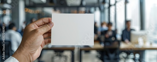 Hand displaying a blank card against a busy office backdrop photo