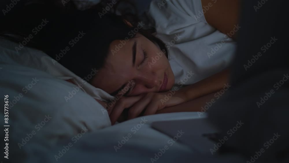 A woman peacefully sleeping next to an open laptop on a bed, illuminated by soft light in a dark room. A woman peacefully sleeping next to an open laptop on a bed, illuminated by soft light in a dark room.