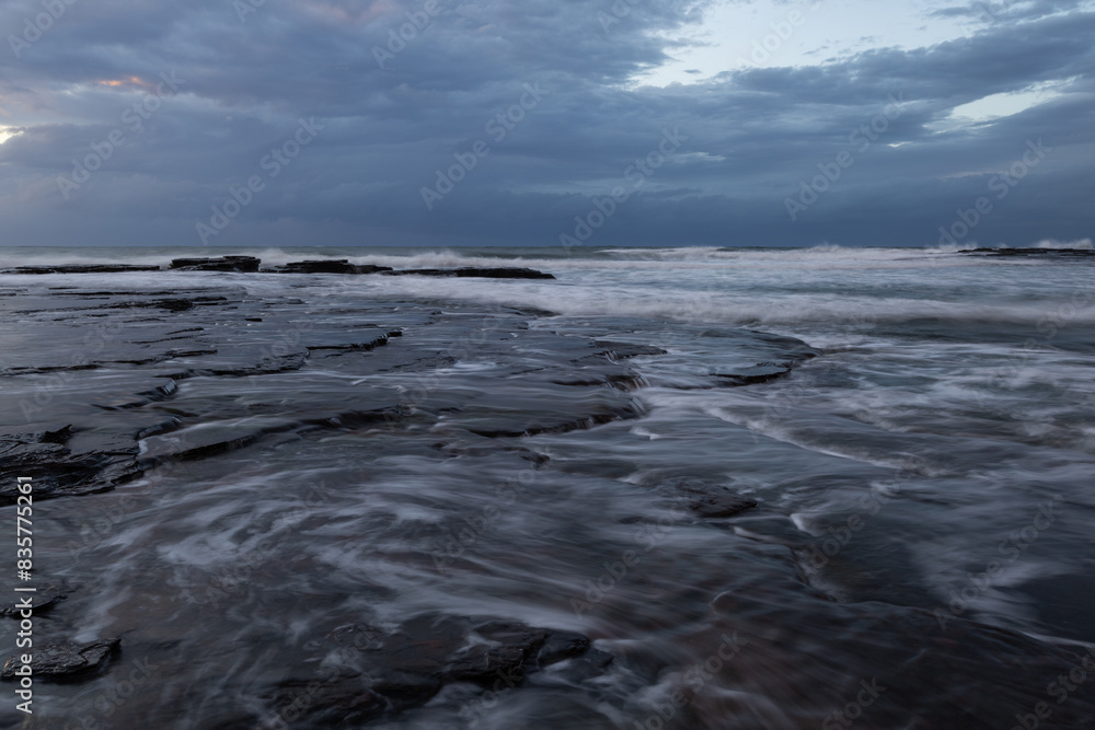 Layer of rock formation on the coast with water flowing.