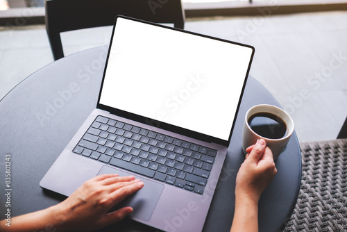 Top view mockup image of a woman working on laptop computer with blank white desktop screen while drinking coffee in cafe
