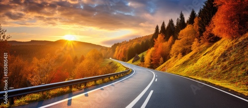 A picturesque autumn scene in the tranquil mountains, showcasing a road meandering through vibrant trees with red and orange leaves at sunset, perfect for a scenic travel journey. Copy space image