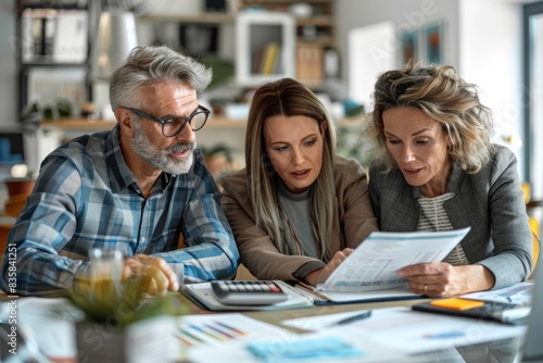 Close-up of a financial advisor explaining tax-saving strategies to a couple. The advisor uses a notepad to highlight key points while the couple reviews the information attentively. The desk is