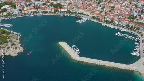 Beautiful coastline, a cozy bay with tourist, moored ships and yachts in the harbor and views of the mountains. Calm beach, traditional boats in Makarska Riviera, Croatia.