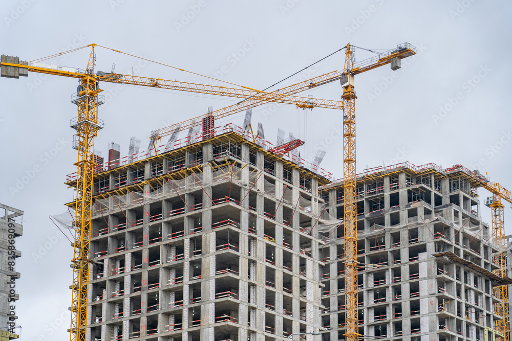 Partially completed, modern apartment building with two construction cranes lifting materials Partially completed, modern apartment building with two construction cranes lifting materials