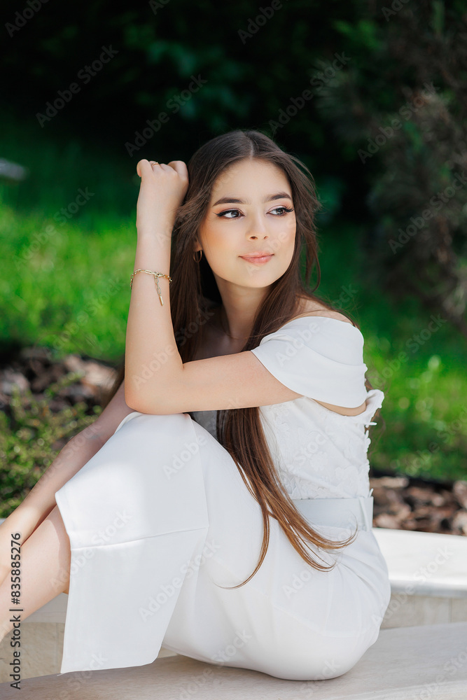 Naklejka premium A woman in a white dress is sitting on a stone ledge. She has her arm around her waist and is smiling