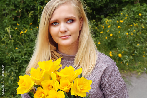 girl with a bouquet. beautiful blonde girl stands in nature with a large bouquet of yellow flowers, close-up nature concept