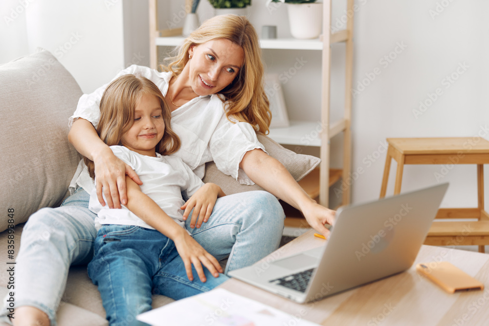 Mother and child bonding on the couch while exploring educational content together on a laptop in a cozy living room Mother and child bonding on the couch while exploring educational content together on a laptop in a cozy living room