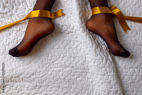 Women's feet on the white bed in black tights with gift ribbon