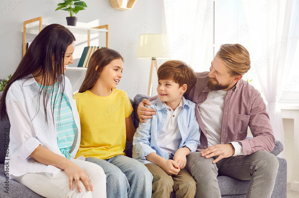 Happy Caucasian family with children sits on the sofa at home, smiling and enjoying themselves. The parents, mother, and father, engage with their children in a moment of joy and fun. Happy Caucasian family with children sits on the sofa at home, smiling and enjoying themselves. The parents, mother, and father, engage with their children in a moment of joy and fun.