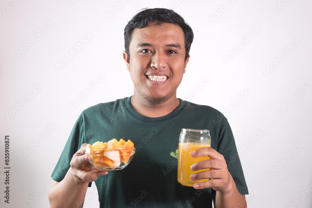 Enjoy healthy food. Handsome young asian man eating fruit salad and orange juice, smiling while standing on white background Enjoy healthy food. Handsome young asian man eating fruit salad and orange juice, smiling while standing on white background