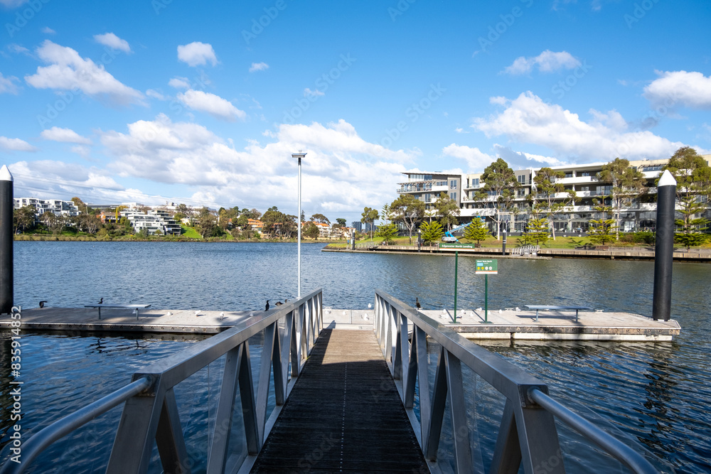 Obraz premium A public floating pontoon at Maribyrnong River with residential apartments and a walkway at the waterfront. Beautiful and well-maintained community facilities in Melbourne's suburban neighborhood.