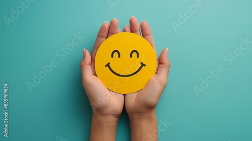 Woman's hands holding a smiley face paper cut on a blue background. Positive and happy concept. Girl's hand holding a round paper in the shape of a happy face on a blue wall. Top view.