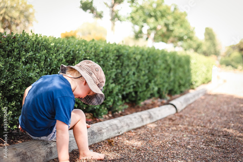 Toddler boy sitting on garden edge at the park with copy space photo