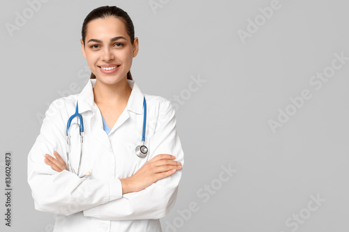 Portrait of young female doctor with stethoscope on grey background