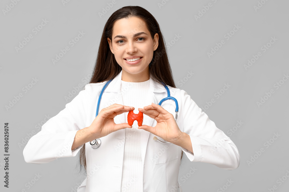 Portrait of female doctor with thyroid model on grey background Portrait of female doctor with thyroid model on grey background