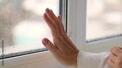 Woman checking with her hand cold draft from the glasses of window. Condensation on the windows glass. 4K