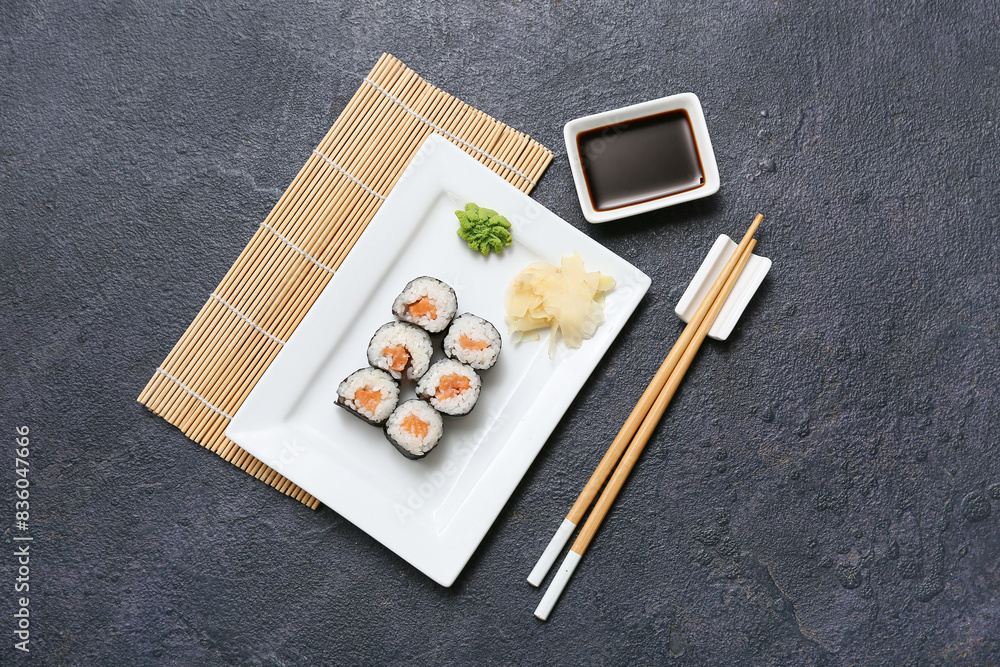 Tasty sushi rolls with soy sauce, chopsticks and bamboo mat on black grunge background Tasty sushi rolls with soy sauce, chopsticks and bamboo mat on black grunge background