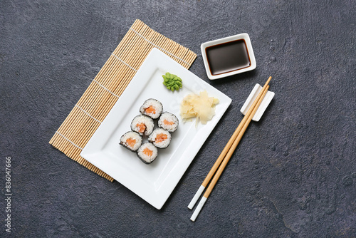 Tasty sushi rolls with soy sauce  chopsticks and bamboo mat on black grunge background