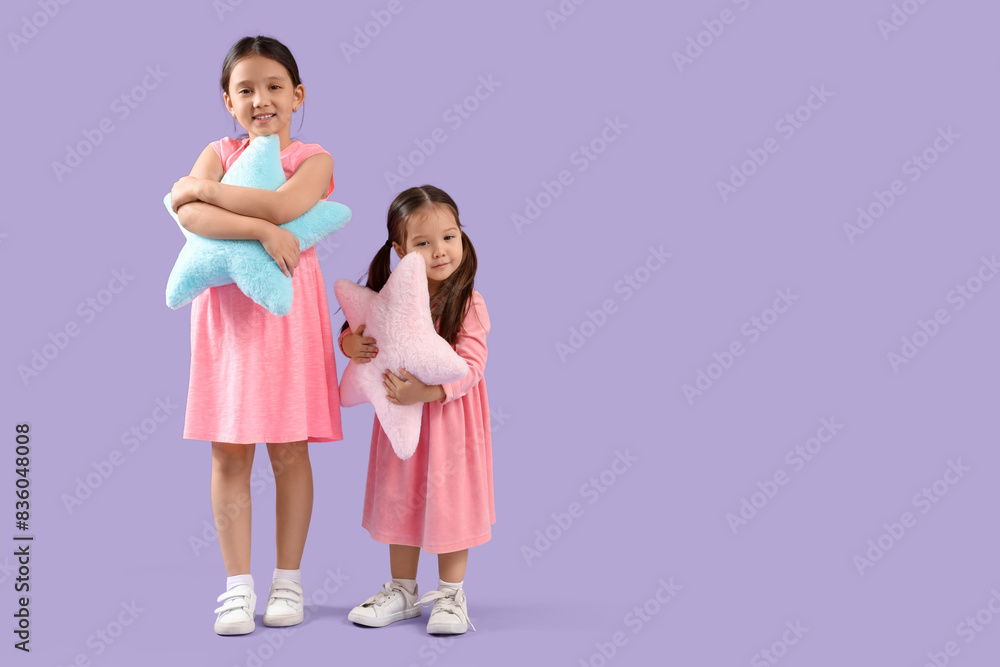 Cute little Asian happy sisters with pillows in shape of stars on purple background Cute little Asian happy sisters with pillows in shape of stars on purple background