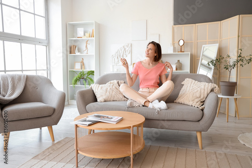 Smiling young woman with air conditioner remote control sitting on sofa in living room