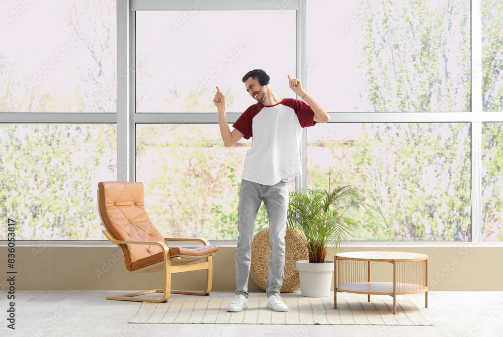 Young bearded man in headphones dancing near window at home Young bearded man in headphones dancing near window at home