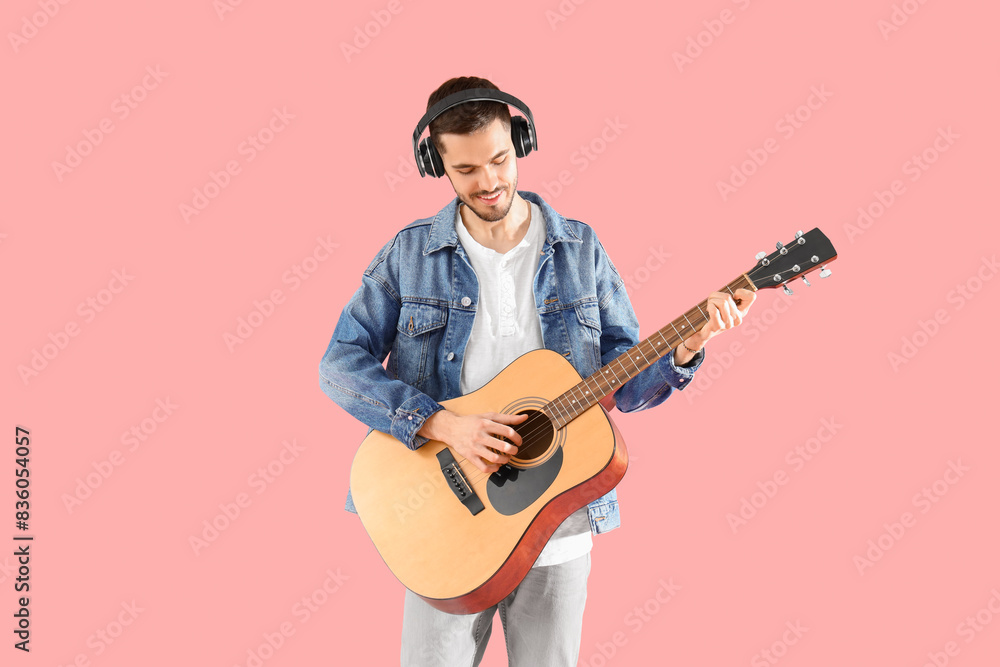 Young bearded man in headphones playing guitar on pink background Young bearded man in headphones playing guitar on pink background