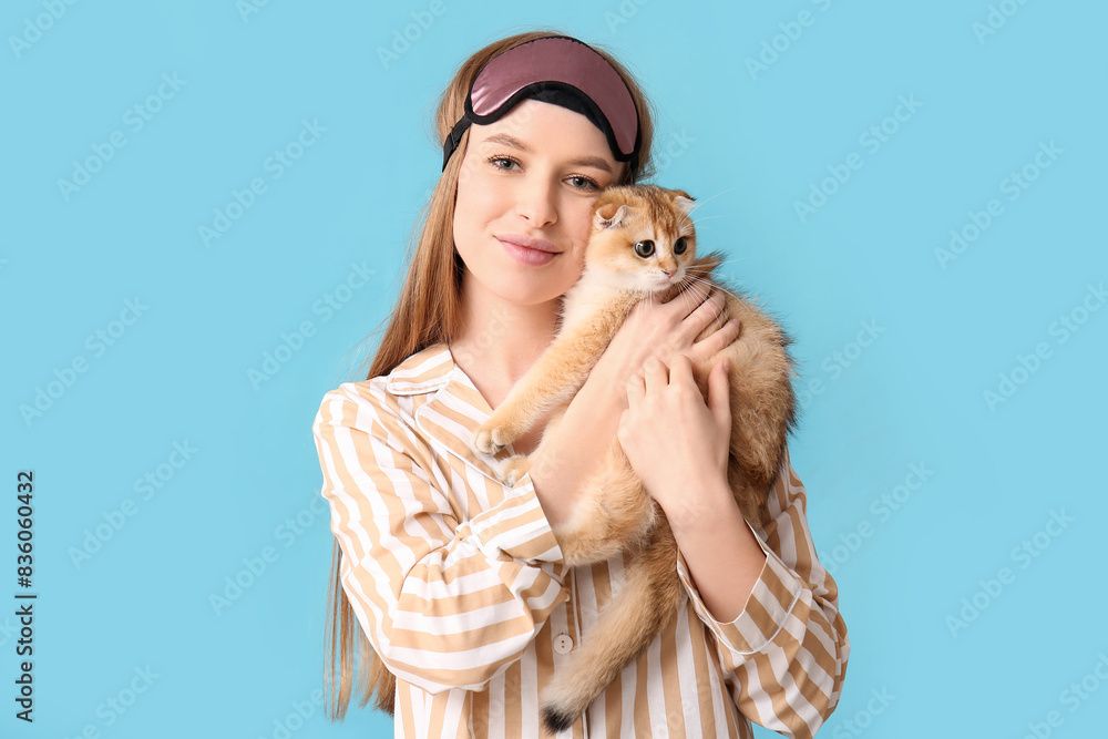 Young woman in pajamas with cute kitten on blue background Young woman in pajamas with cute kitten on blue background
