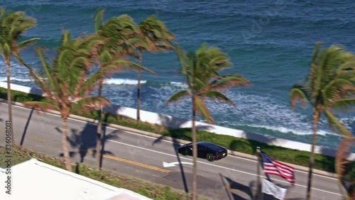 Establishing aerial rolling shot of supercar driving in Miami West Palm Beach on a sunny day. Epic drone footage of supercar driving on Miami Sunny Streets