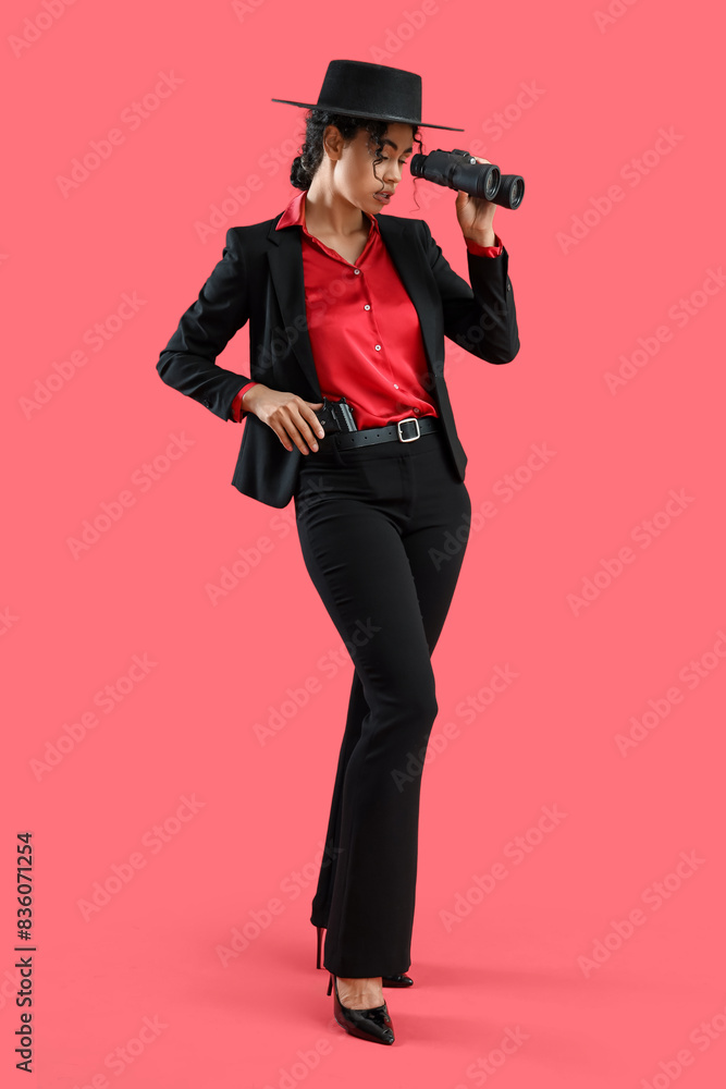 Female African-American spy with binoculars and gun on red background Female African-American spy with binoculars and gun on red background
