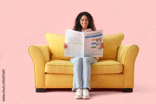 Free Download Young African-American woman reading newspaper on yellow sofa against pink background - GFXLoad