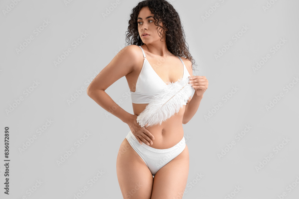 Obraz premium Young African-American woman in underwear with feather on light background