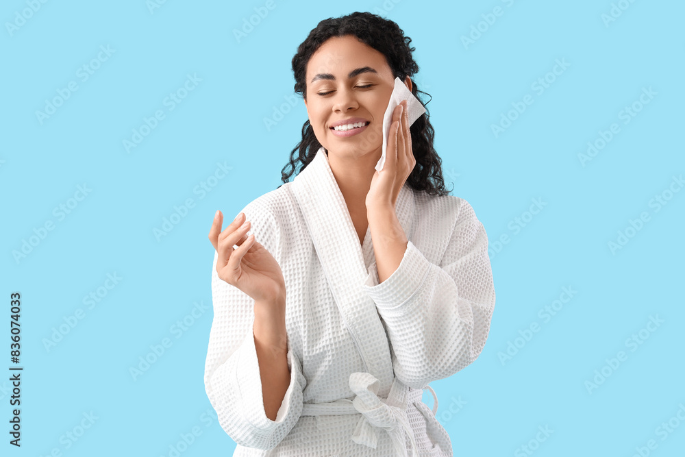 Young African-American woman removing makeup with wipe on blue background Young African-American woman removing makeup with wipe on blue background