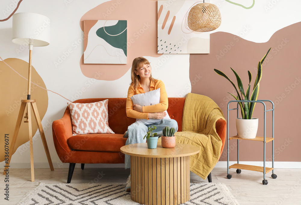 Young woman sitting on sofa with hanging stylish paintings at home Young woman sitting on sofa with hanging stylish paintings at home