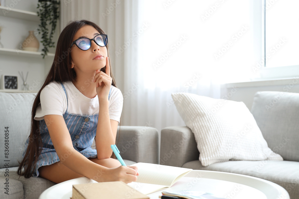 Thoughtful little schoolgirl writing in copybook on sofa at home Thoughtful little schoolgirl writing in copybook on sofa at home