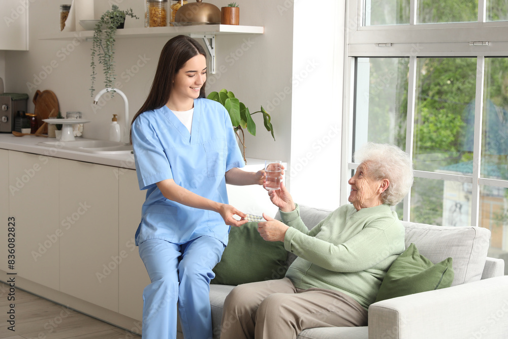 Young nurse giving pills and glass of water to senior woman in kitchen Young nurse giving pills and glass of water to senior woman in kitchen