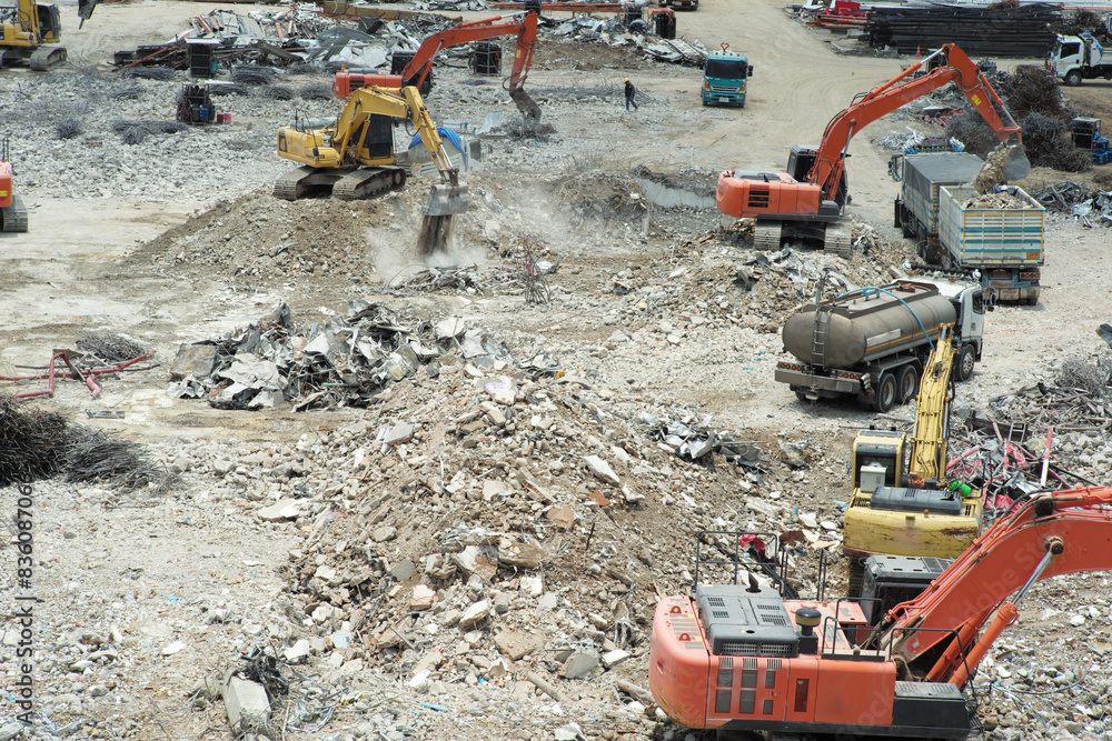 Many excavators working on the ground of the construction site while removing the salvage after the destruction of the building Many excavators working on the ground of the construction site while removing the salvage after the destruction of the building