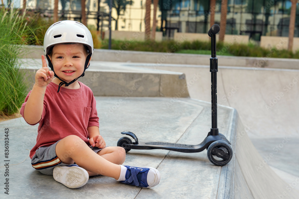 Obraz premium little boy wearing a helmet and with his scooter in a skate park
