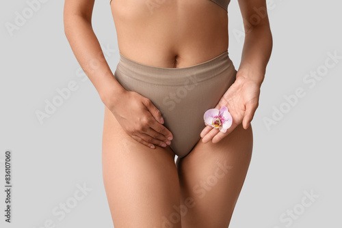 Beautiful young African-American woman in panties with orchid flower on grey background, closeup