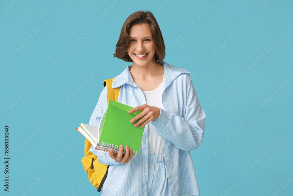 Beautiful female student with backpack and notebooks on blue background Beautiful female student with backpack and notebooks on blue background