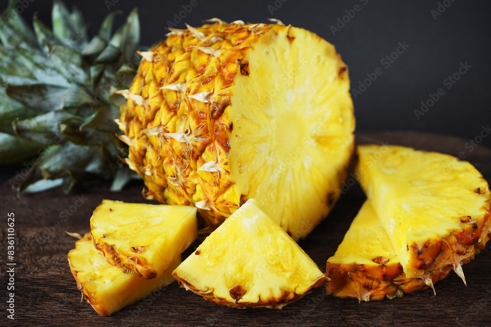 Ripe juicy pineapple next to cut pieces on a wooden board on a dark background Ripe juicy pineapple next to cut pieces on a wooden board on a dark background