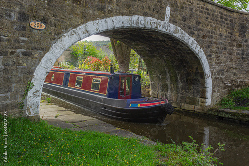 Bild auf Leinwand A colourful canal boat emerges from under an old stone bridge on the Leeds and L