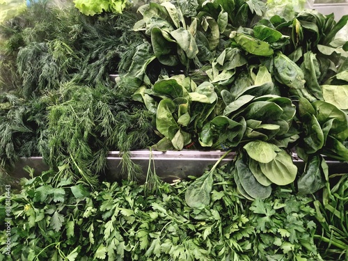 in a grocery supermarket, there is a variety of greens on the counter for cooking; moist steam from an air humidifier is used to preserve freshness