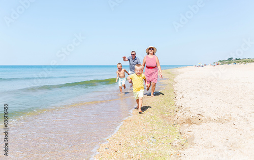 An elderly man, woman and children are running along the sandy seashore on a sunny day. Happy grandparents with grandchildren. Love and tenderness. Active holiday with family.