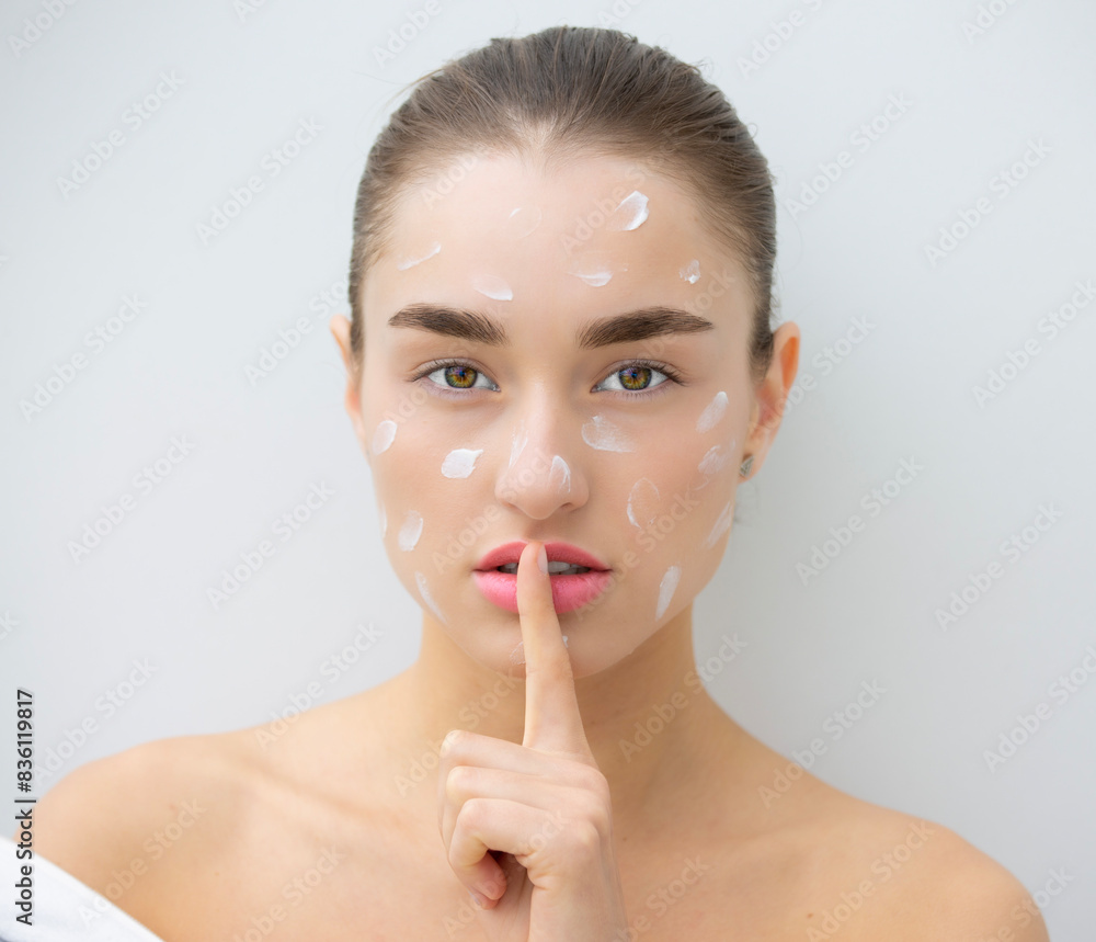 Portrait of a beautiful woman with cream applied to face showing finger to lips gesture Portrait of a beautiful woman with cream applied to face showing finger to lips gesture