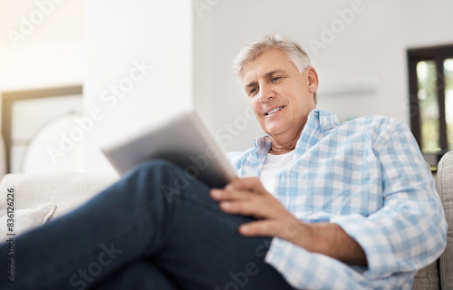 Smile, tablet and mature man on sofa for communication, networking or reading news article in living room. Online, technology and person for watching video, browsing internet or social media in home © peopleimages.com