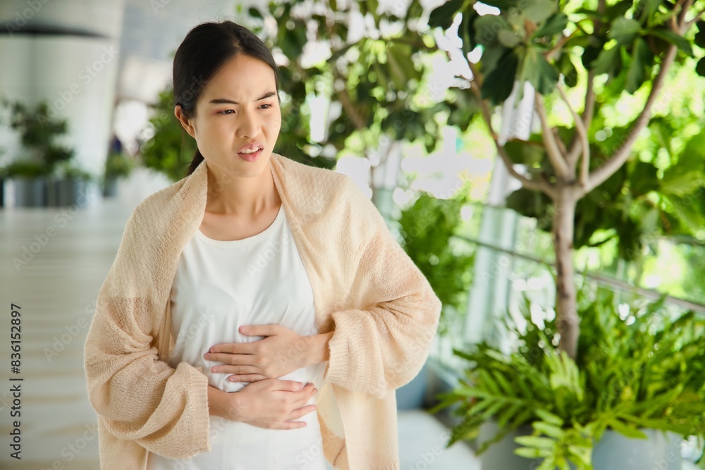 Asian woman with stomach ache, concept image of menstrual period cramp, abdominal pain, food poisoning, gastritis, acid reflux or colon cancer
