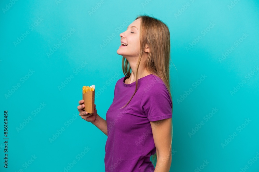Young Russian woman catching french fries isolated on blue background laughing in lateral position Young Russian woman catching french fries isolated on blue background laughing in lateral position