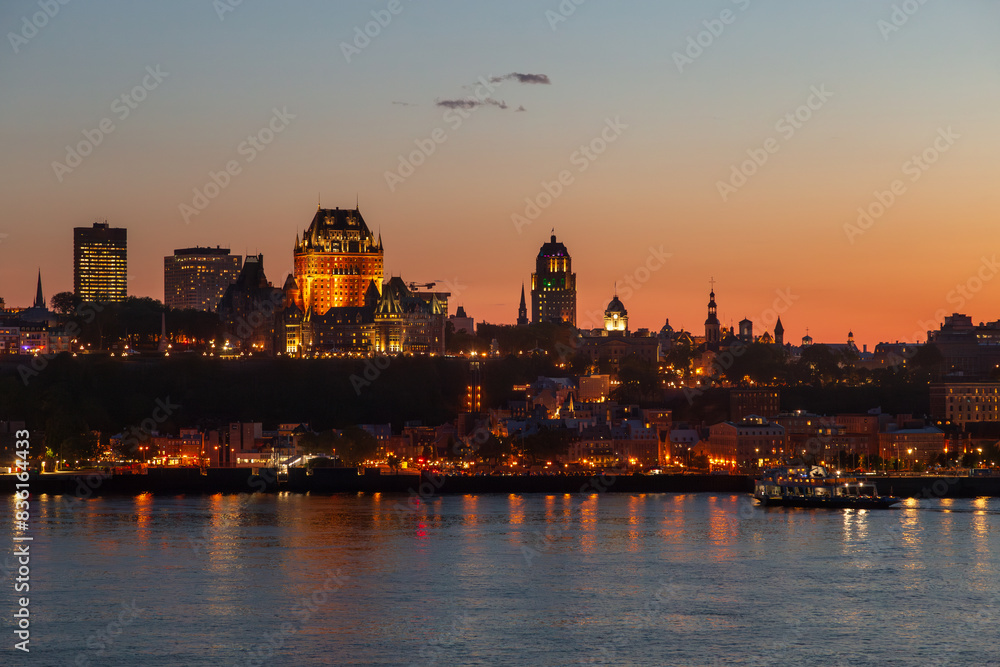 Obraz premium The Quebec City skyline and its illuminated buildings seen at dusk from Lévis, with the St. Lawrence River in the foreground