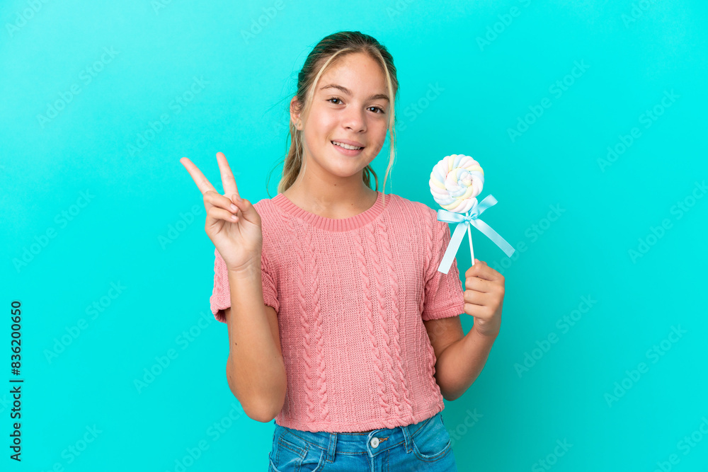 Little Caucasian girl holding a lollipop isolated on blue background smiling and showing victory sign Little Caucasian girl holding a lollipop isolated on blue background smiling and showing victory sign